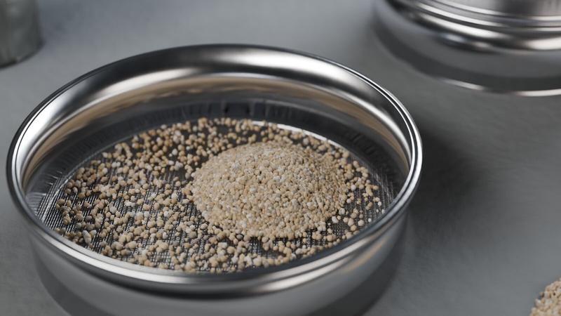 Tamis d’analyse en inox avec des grains de sable retenus sur la toile, autres tamis en arrière-plan